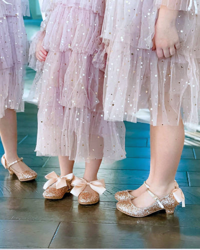 Children wearing sparkly dresses and glitter shoes on a wooden floor.